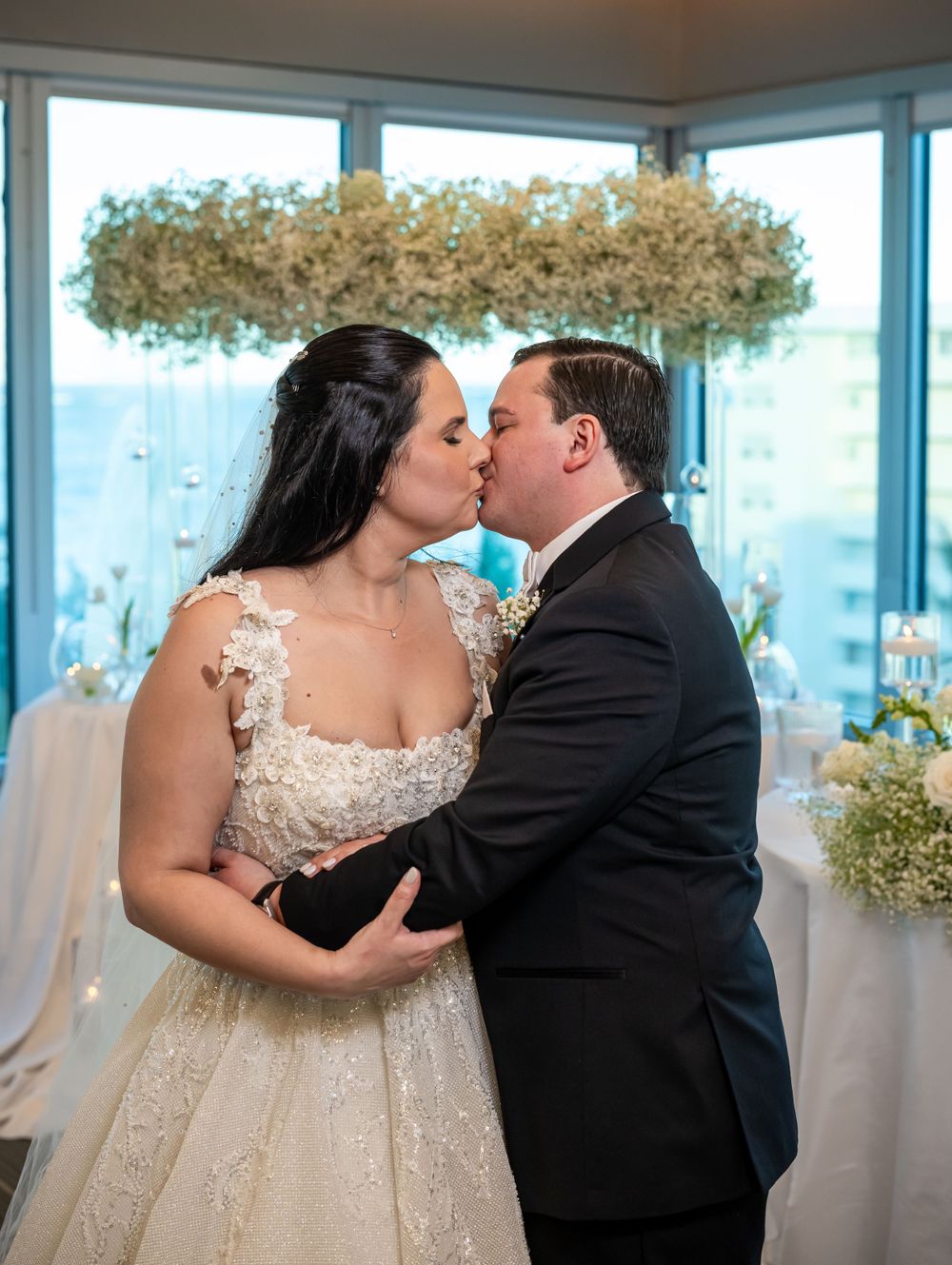 An intimate wedding moment captured beneath a suspended baby's breath floral arrangement.
