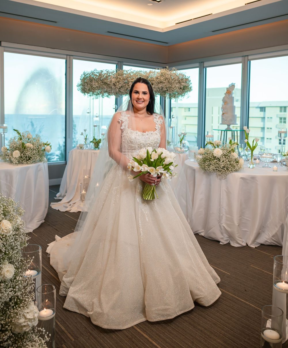 A wedding reception space with white decor, floor-to-ceiling windows, and a suspended floral arrangement.