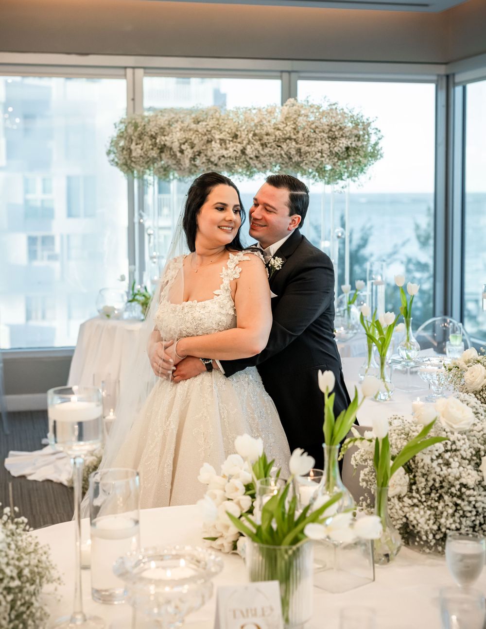 An elegant wedding reception with white floral arrangements and modern clear chairs.