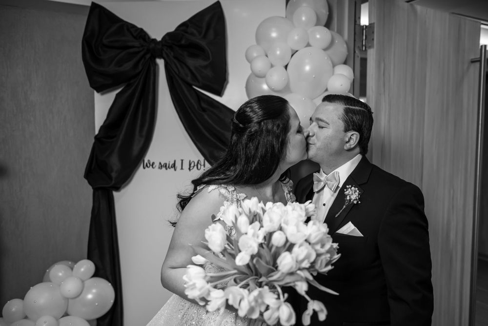 A romantic black and white wedding photo showing a couple kissing while holding a bouquet of white flowers.