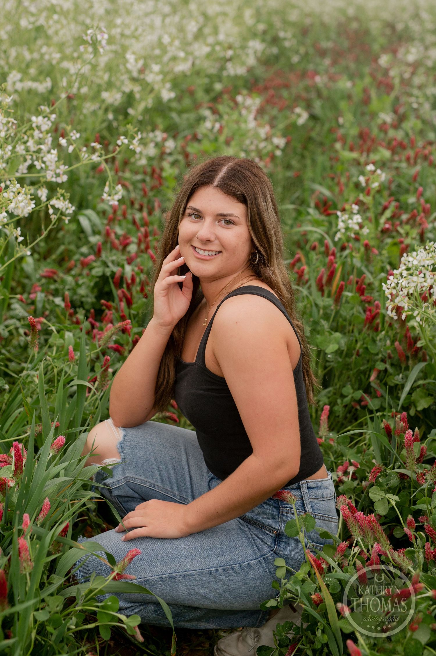 Candid portrait sitting among blooming wildflowers in a field wearing casual summer attire.