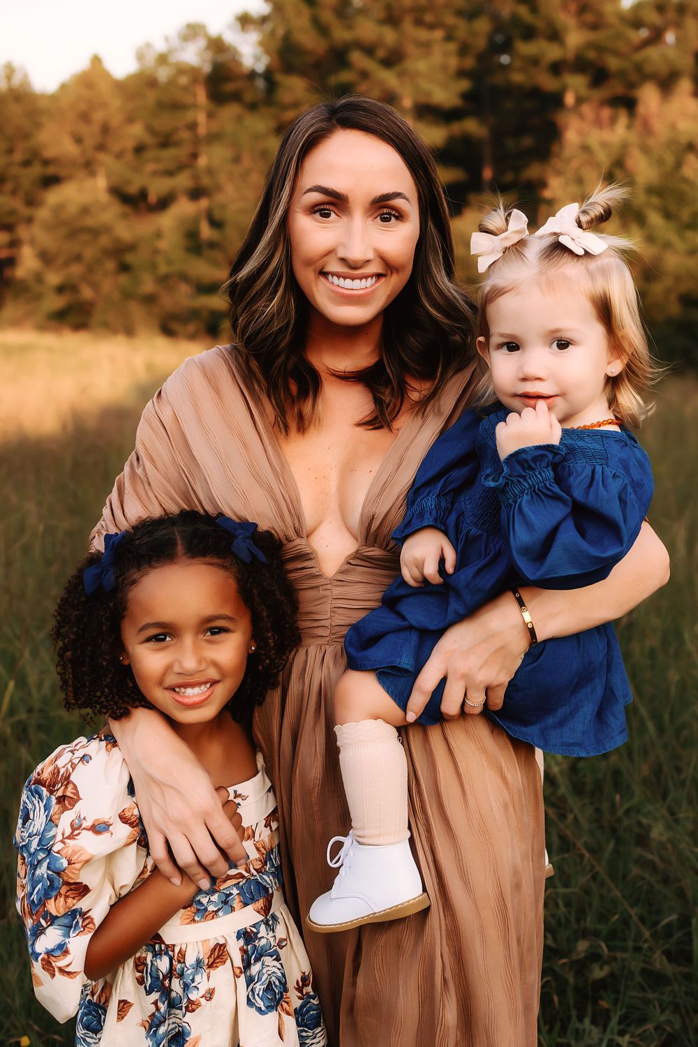 Three people pose together outdoors in coordinated outfits with warm neutral and blue tones during sunset.