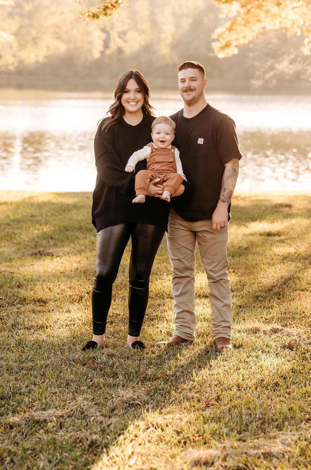 Family standing together by a lake at sunset with golden light streaming through trees in the background.