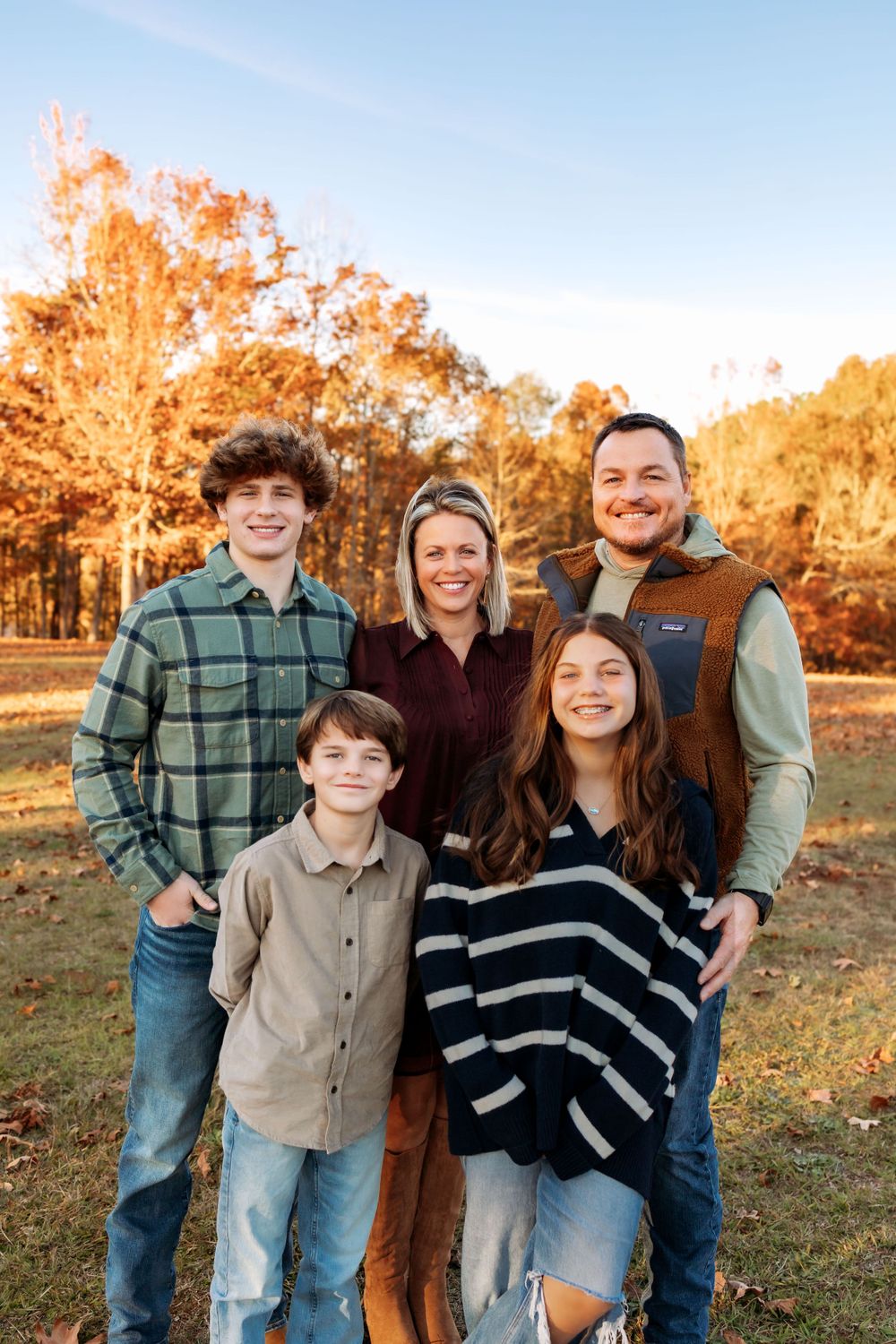 A family poses together outdoors during autumn with colorful fall foliage in the background.