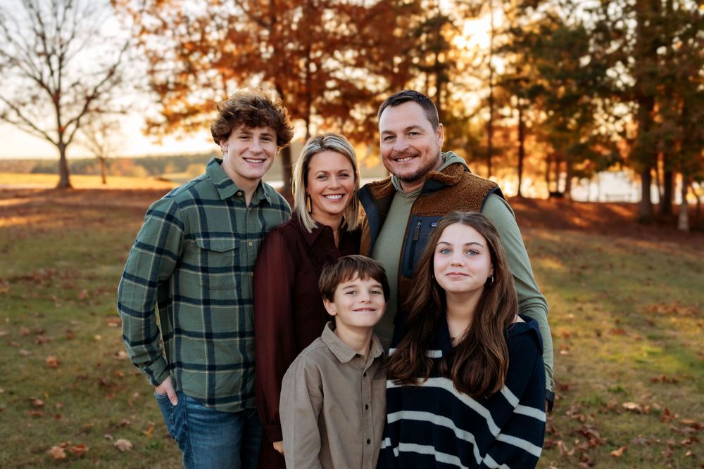 A family of five stands together outdoors during golden hour sunset with trees in the background.