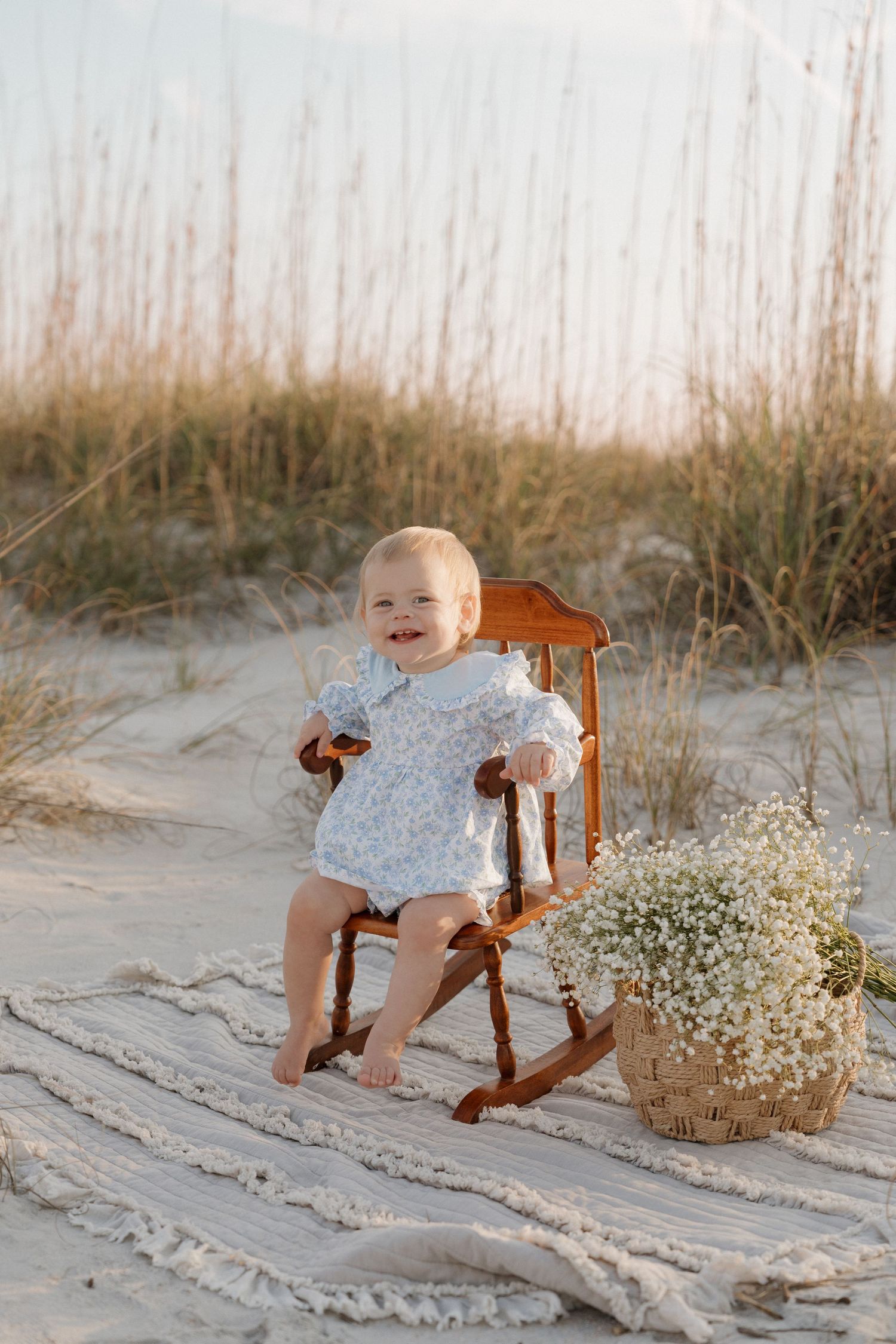 A series of photos showing a small child in a white dress sitting in a wooden rocking chair on a sandy beach with flowers.