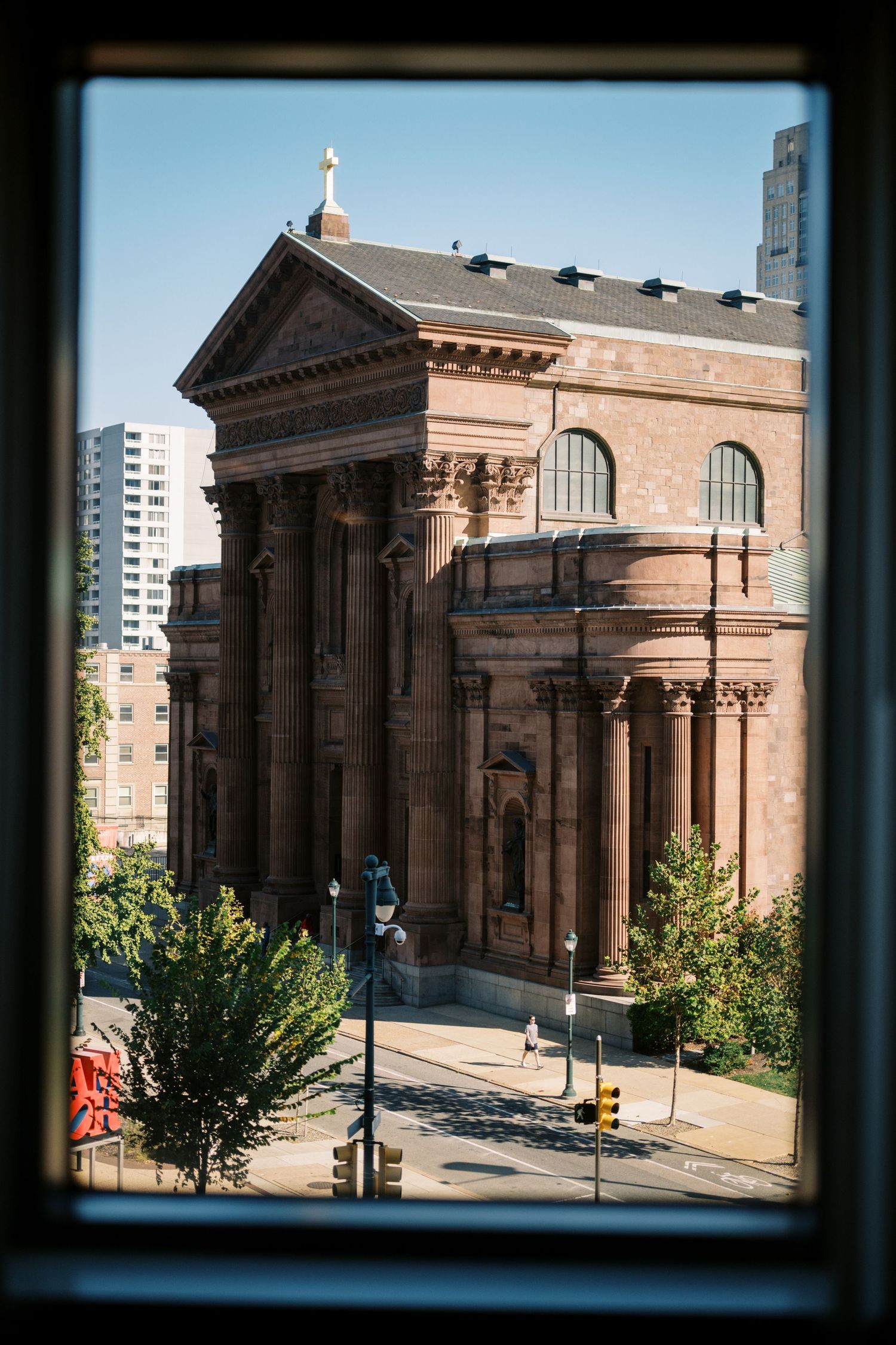 View through window of historic brick church with classical columns and arched windows in urban setting.