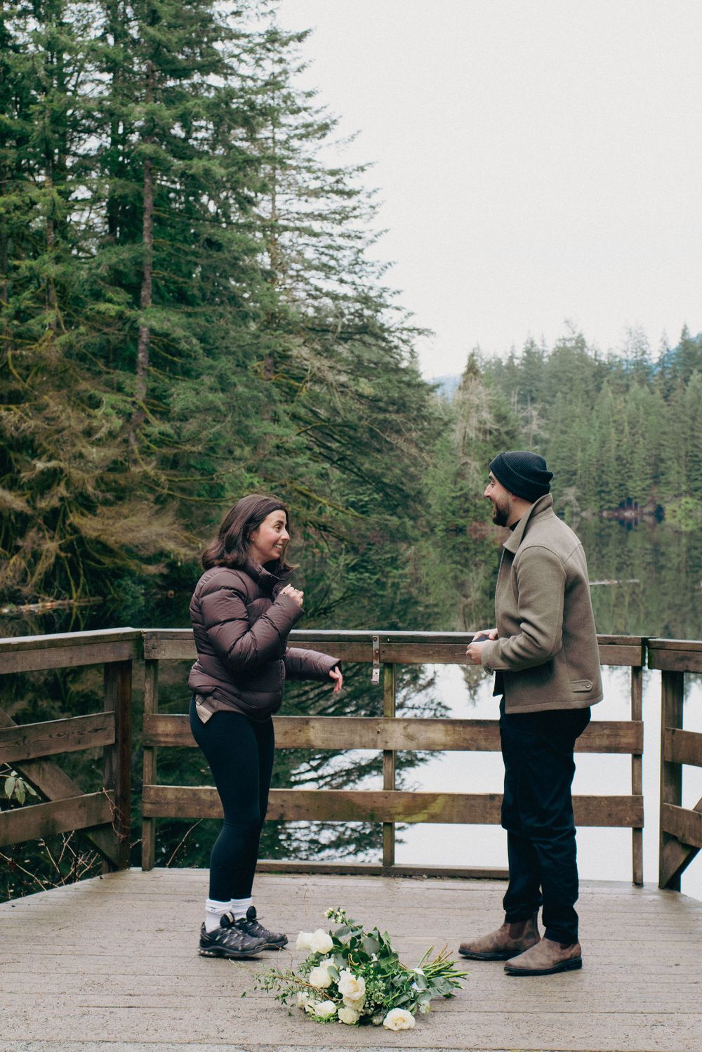 A surprise proposal moment captured on a wooden deck with white flowers and mountain scenery.