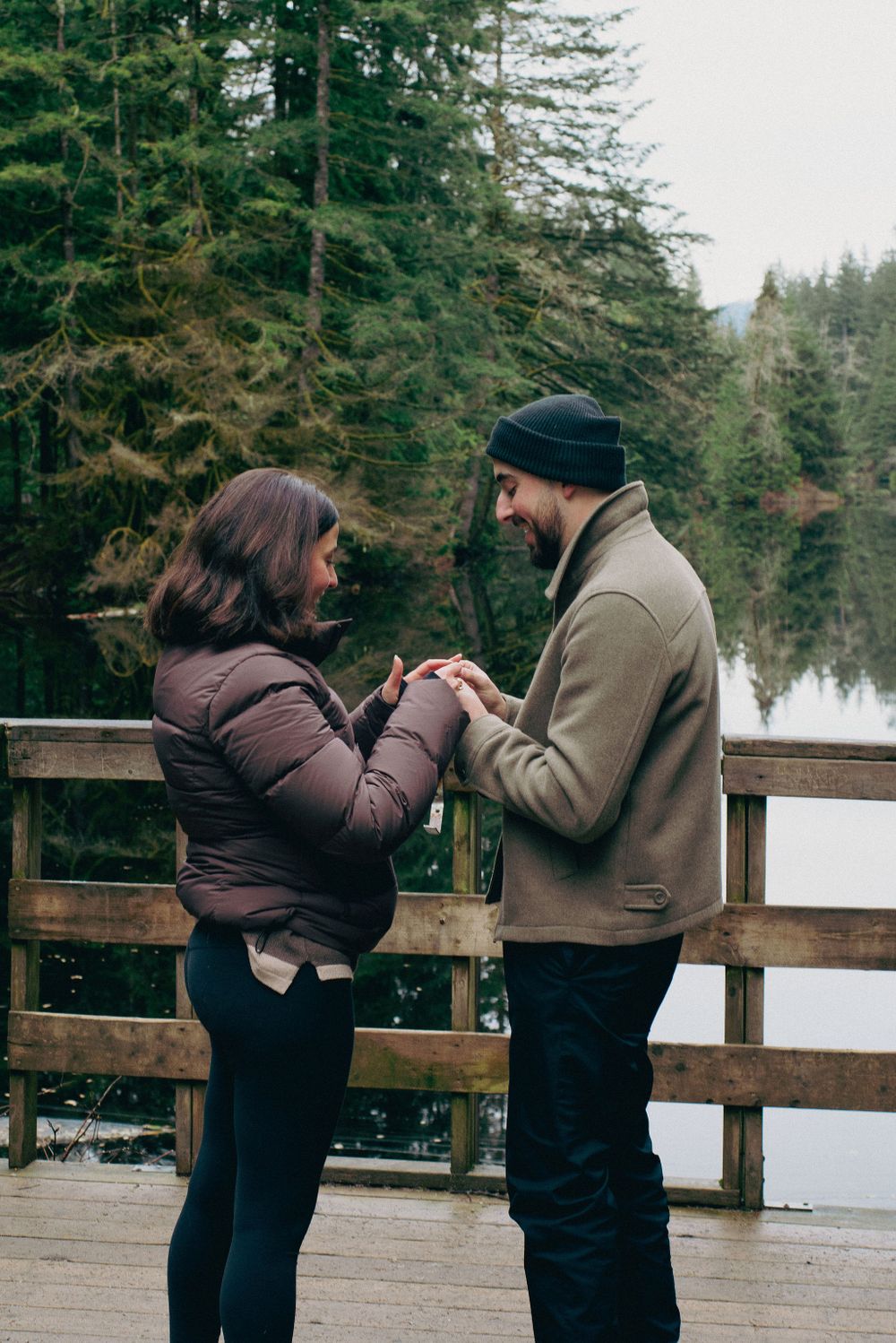 A winter marriage proposal takes place on a wooden observation deck with snow-capped trees in background.
