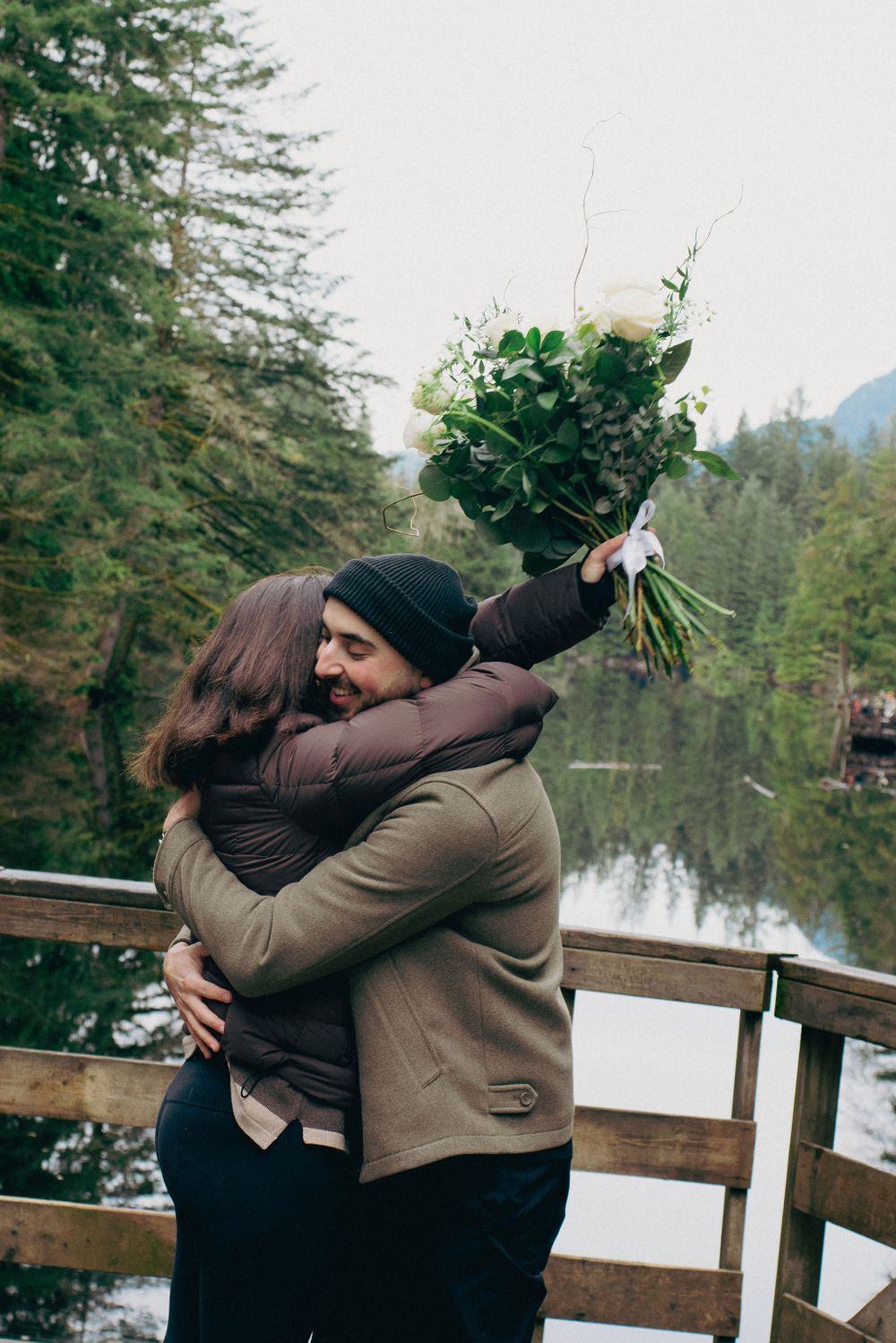 An intimate embrace follows a winter proposal moment on a scenic mountain overlook.