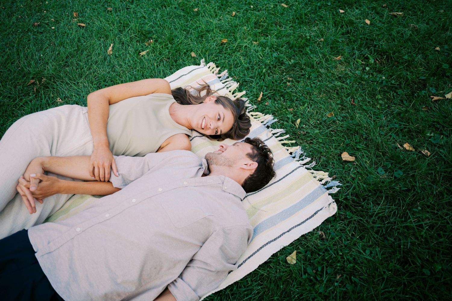 A couple lying together on a blanket in the grass on a sunny day, sharing an intimate moment of rest.