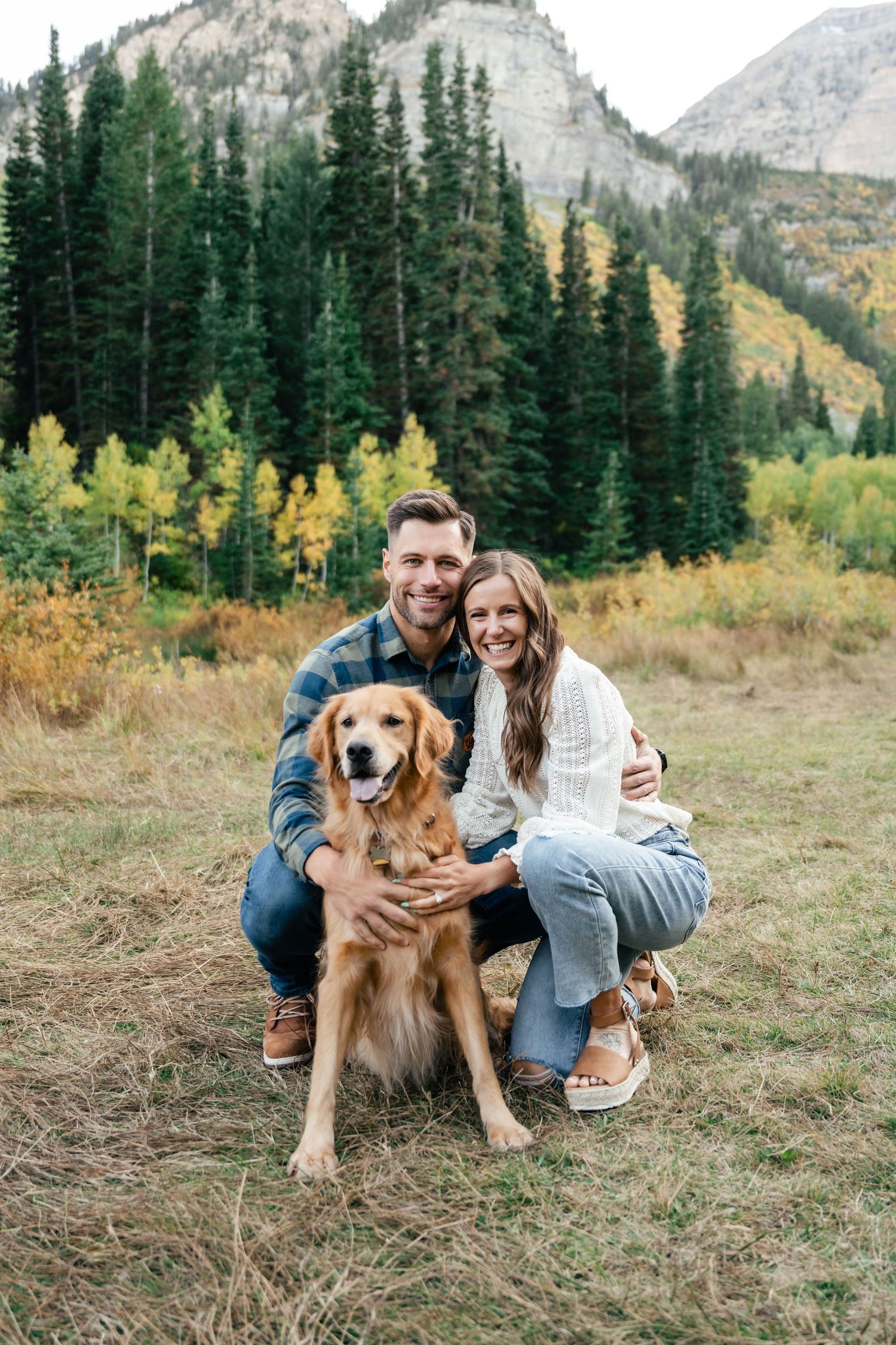 A Golden Retriever and couple smile in evergreen trees and fall foliage during their engagement session. Utah Wedding Photographer. Engaged.