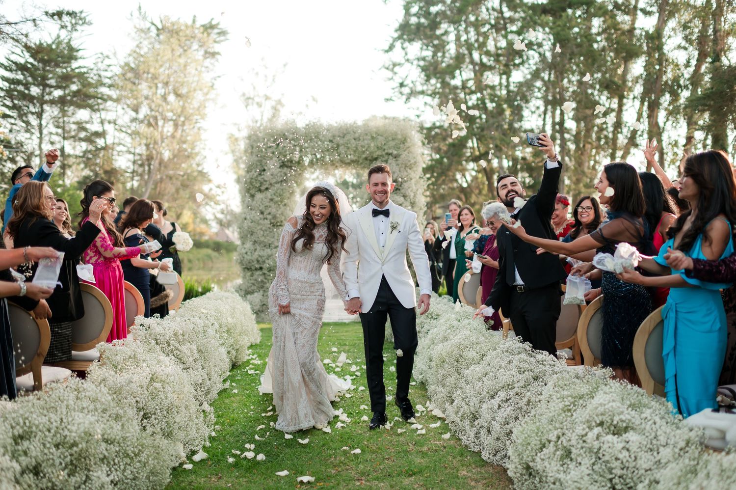 Outdoor wedding ceremony setup with white floral arrangements and gathered guests.