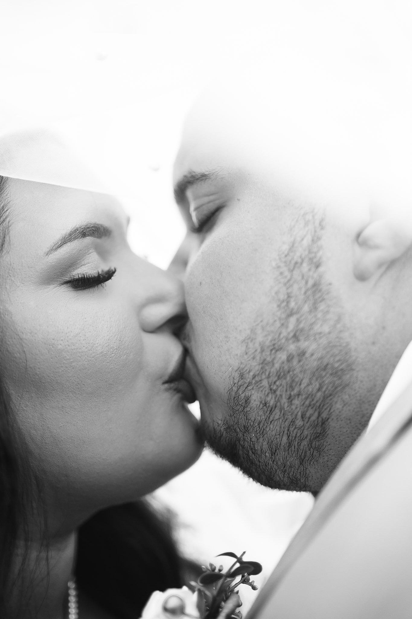 A loving couple in formal wedding attire share an intimate moment on elegant stone steps of a grand building entrance.