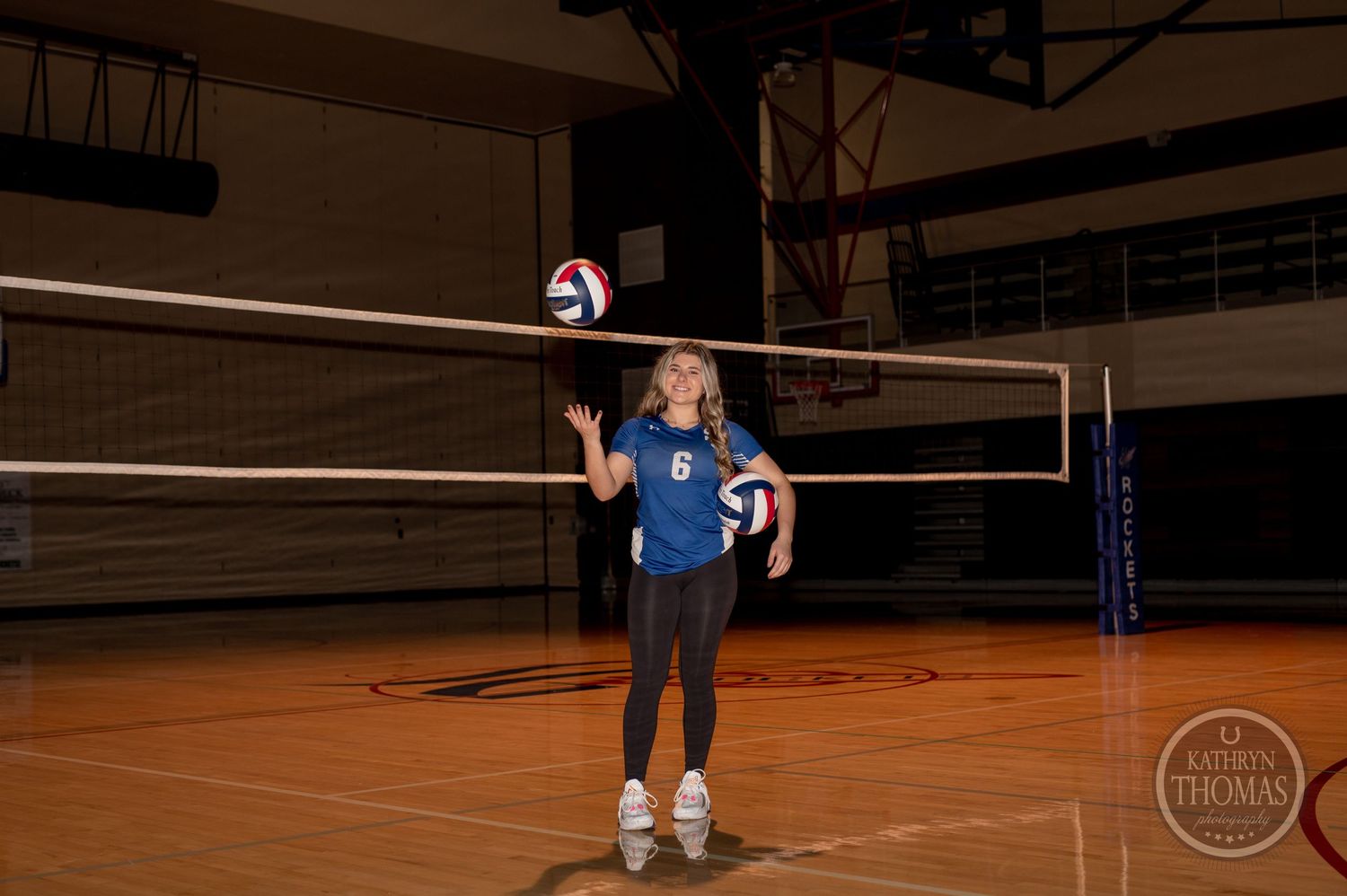Athlete in blue uniform demonstrates volleyball serve position in gymnasium.