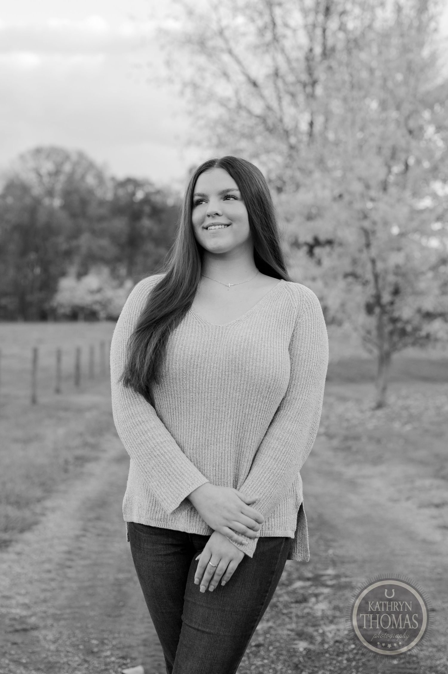 A black and white portrait features a person in a cozy sweater standing on a rural path.