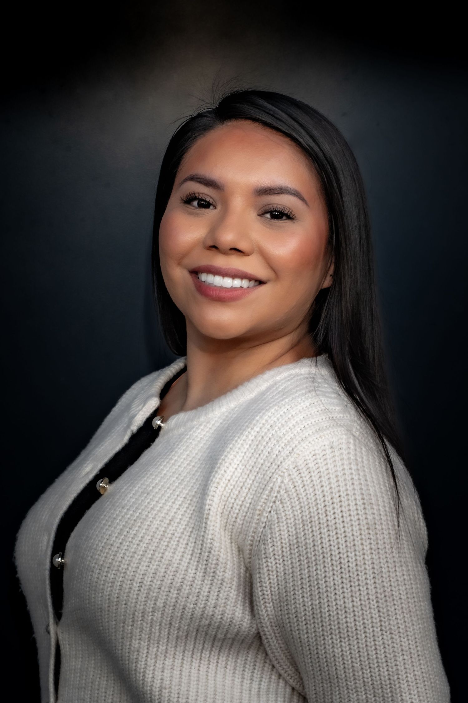 Professional studio portrait against dark background wearing white knit sweater.