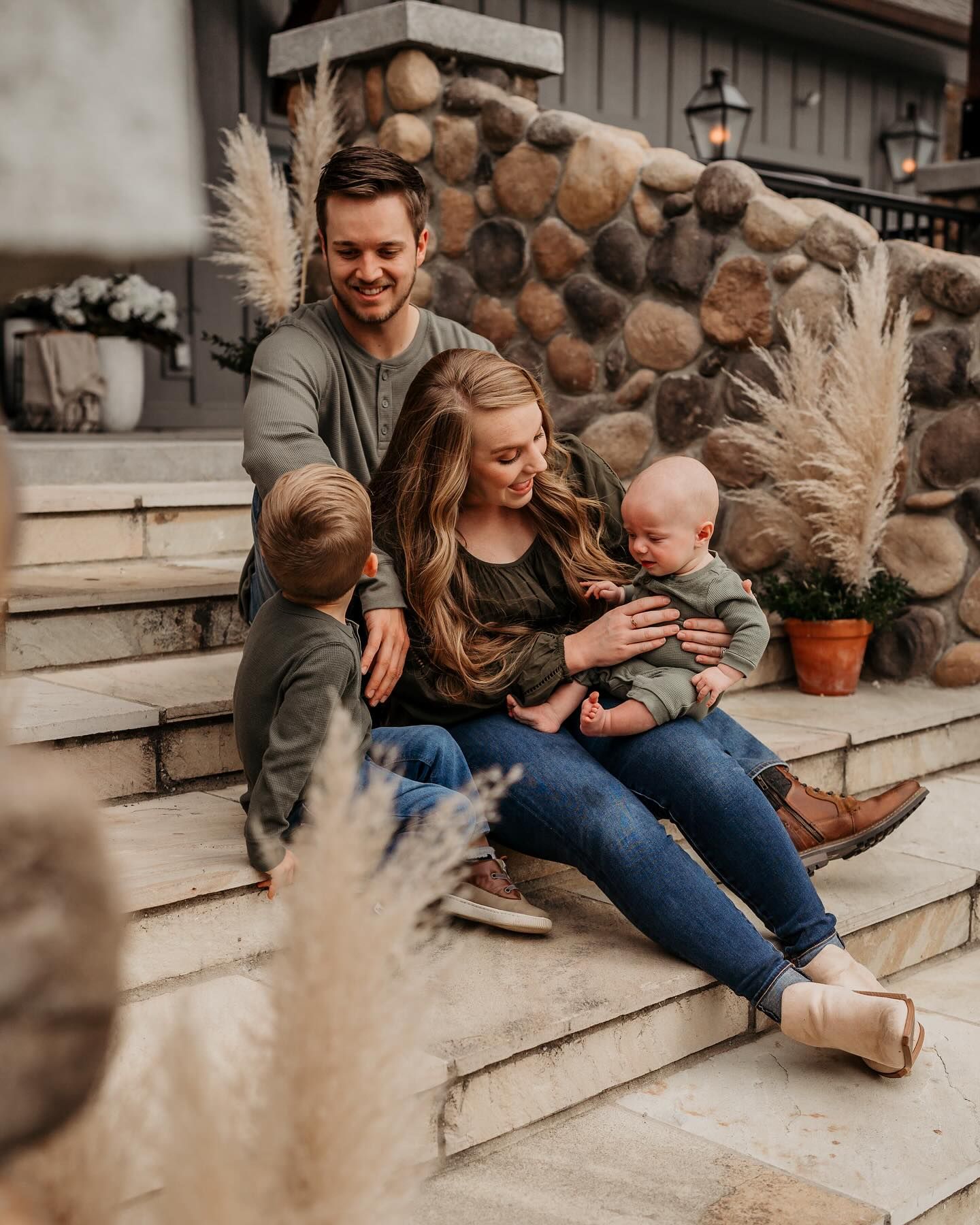 Family sitting together on stone steps surrounded by fall decorative pampas grass.