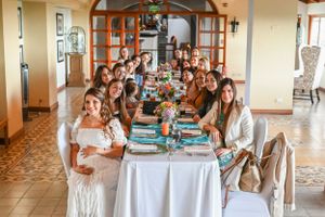 A large group sits together for a formal celebration meal at an elegant white-clothed table decorated in turquoise accents.