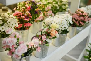 Row of small galvanized metal buckets filled with pink, white and multicolored flowers arranged on a white shelf.