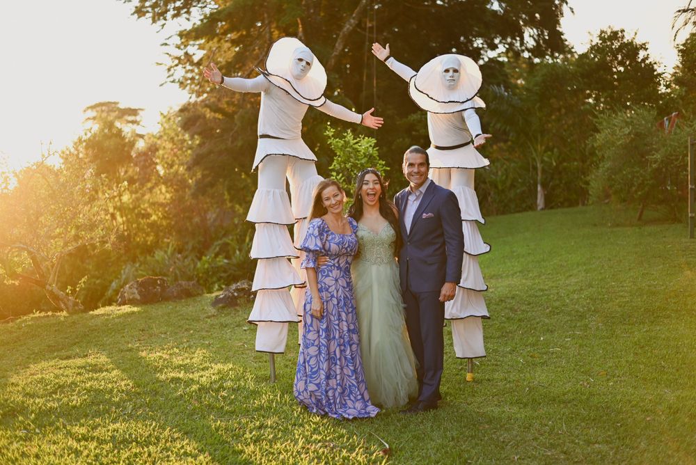 Wedding party poses between two tall stacks of white cowboy hats in a grassy field at sunset.