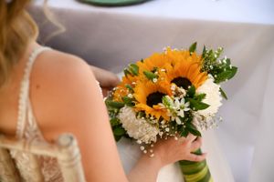A bridal bouquet with bright orange sunflowers and delicate white baby's breath flowers held against a light background.