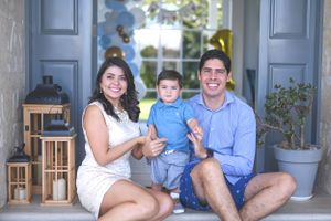 Family sits together on front porch steps with decorative lanterns and potted plants beside doorway.