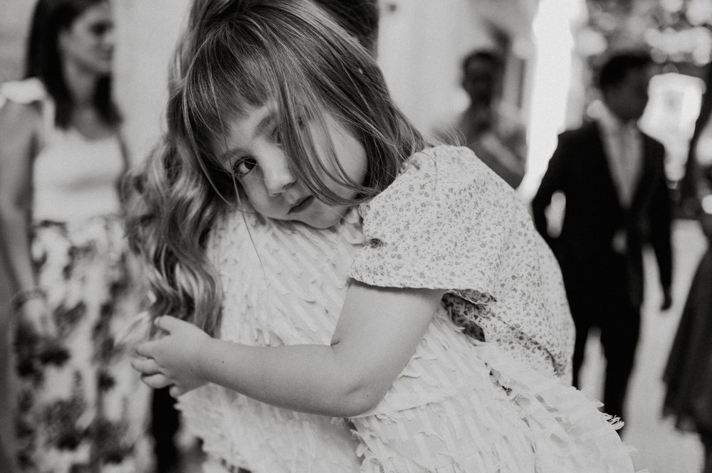 A small child in a white lace dress twirls playfully during a formal event.