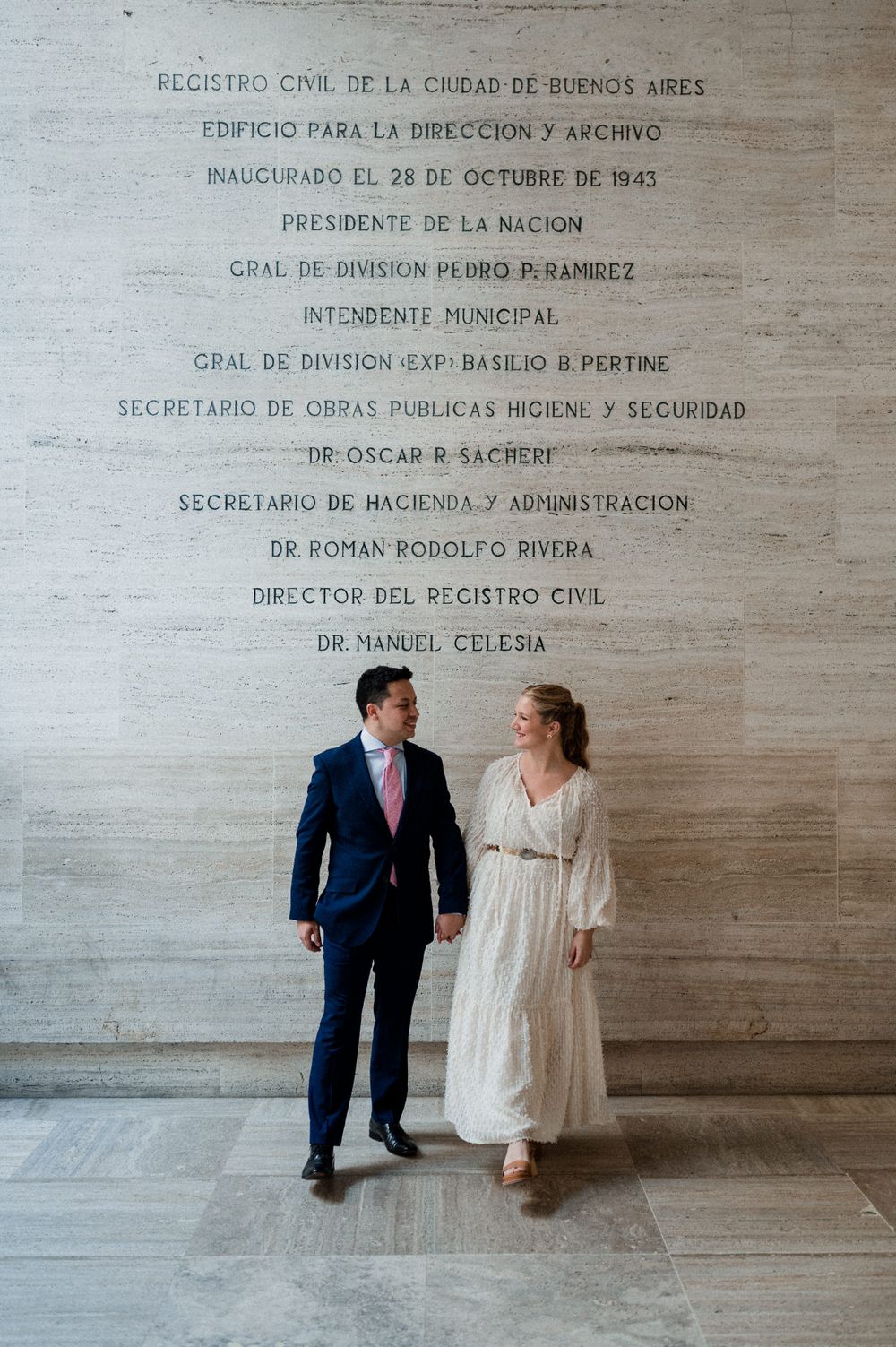 A couple poses against a wall with Spanish text at what appears to be a government building in Buenos Aires.