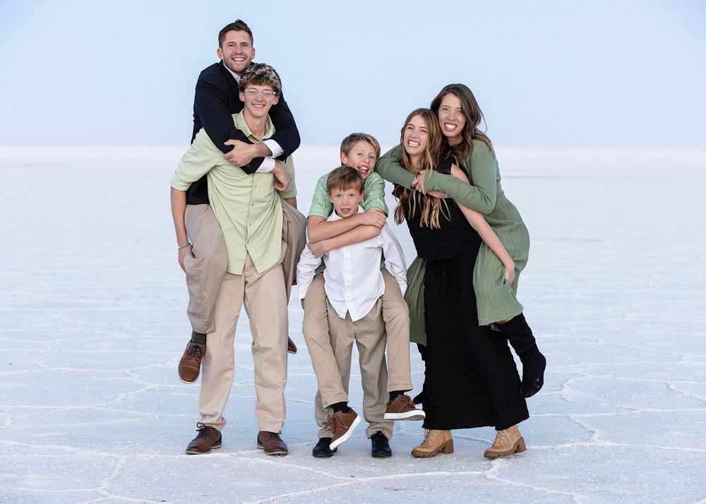 A family photographer takes photo of large family together on white Bonneville salt flats wearing casual clothing in natural lighting.