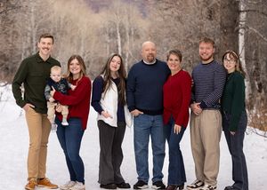 A group of people poses together for a portrait in a snowy winter landscape wearing warm sweaters in red, blue and green.