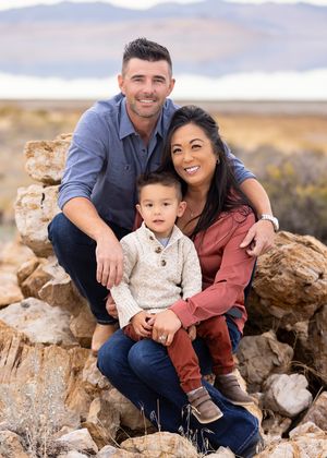 A family poses together for family photographers on rocky terrain with mountains in the background during an outdoor photo session.
