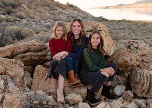 Family sitting together on rocky terrain at sunset in a desert landscape for family photographer.