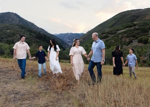 Family photographer near me takes photo of family walking together through a grassy field with mountains in the background