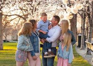 A happy family shares joyful moments together for family photographer near me under blooming cherry blossom trees at sunset in a park.