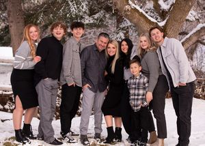 A group of eight people wearing casual clothing pose together in a snowy winter scene with a tree behind them.