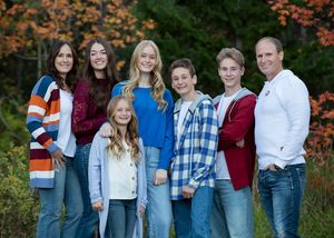 Family group wearing coordinated casual outfits poses together outdoors with colorful autumn foliage in background for family photographer