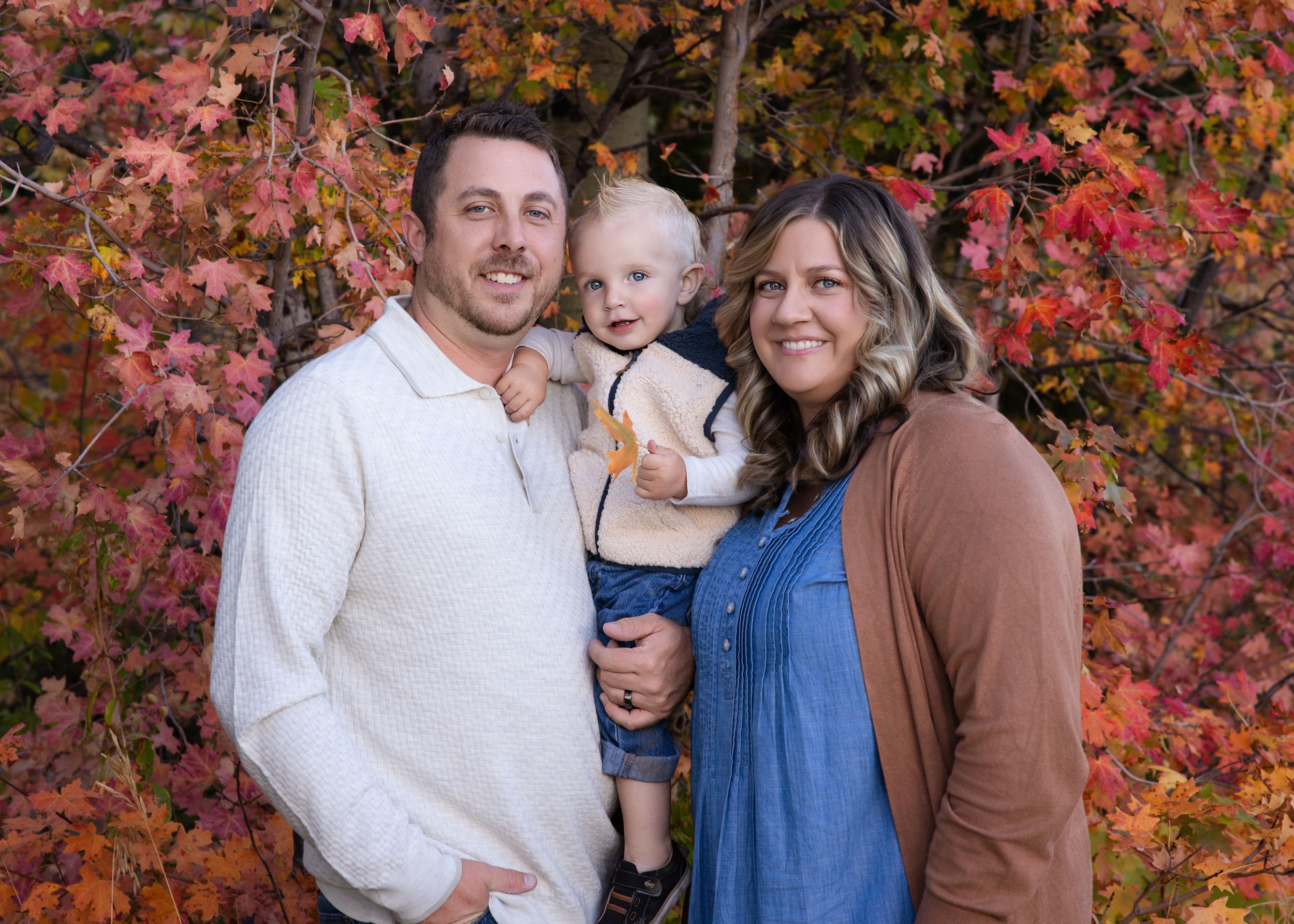 A family poses together against vibrant red autumn foliage in a series of outdoor portrait photographs.