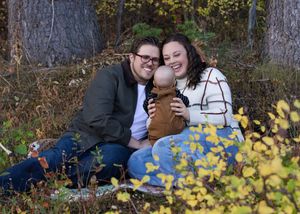 A romantic couple poses for engagement photos among yellow autumn foliage in a natural outdoor setting.