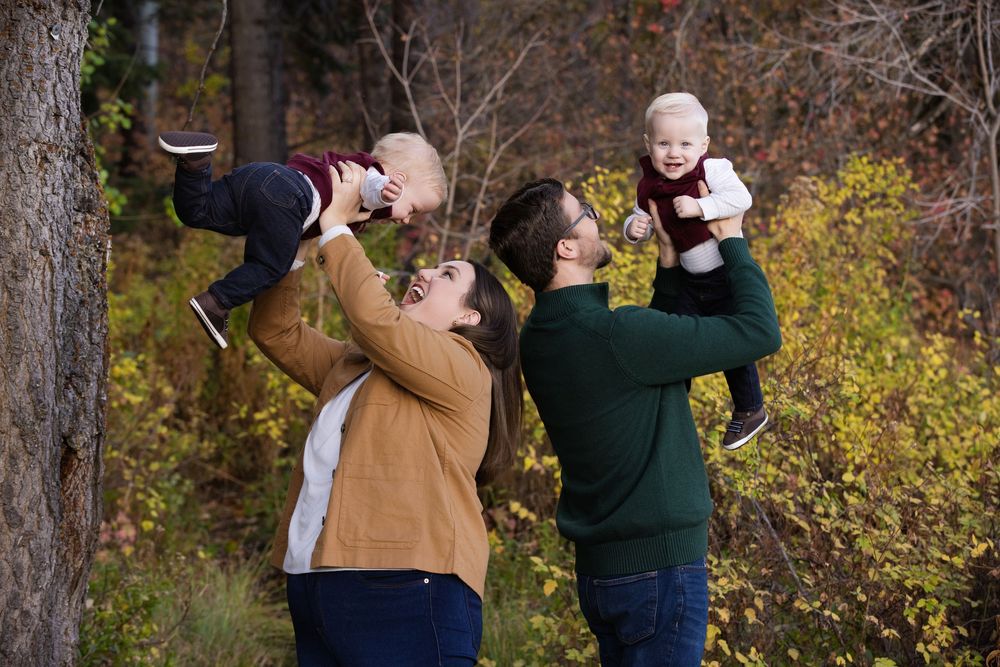 A couple shares tender moments in a wooded autumn setting while taking outdoor photos.