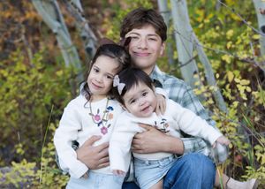 A loving family portrait taken outdoors in autumn with aspen trees and golden foliage in the background.