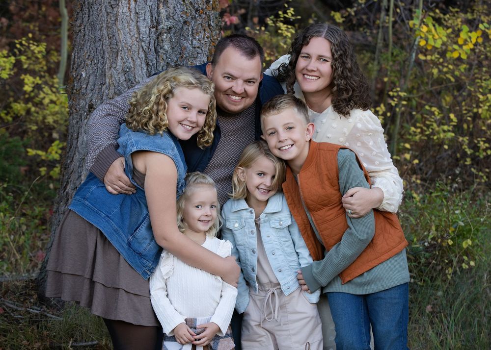 A group of people in coordinating outfits pose together outdoors against an autumn forest backdrop.