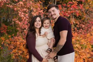 A family poses together against vibrant orange autumn foliage during a fall photo session.
