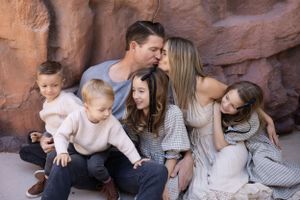 A loving family of six sits together against red rock formations wearing coordinated neutral colored outfits.
