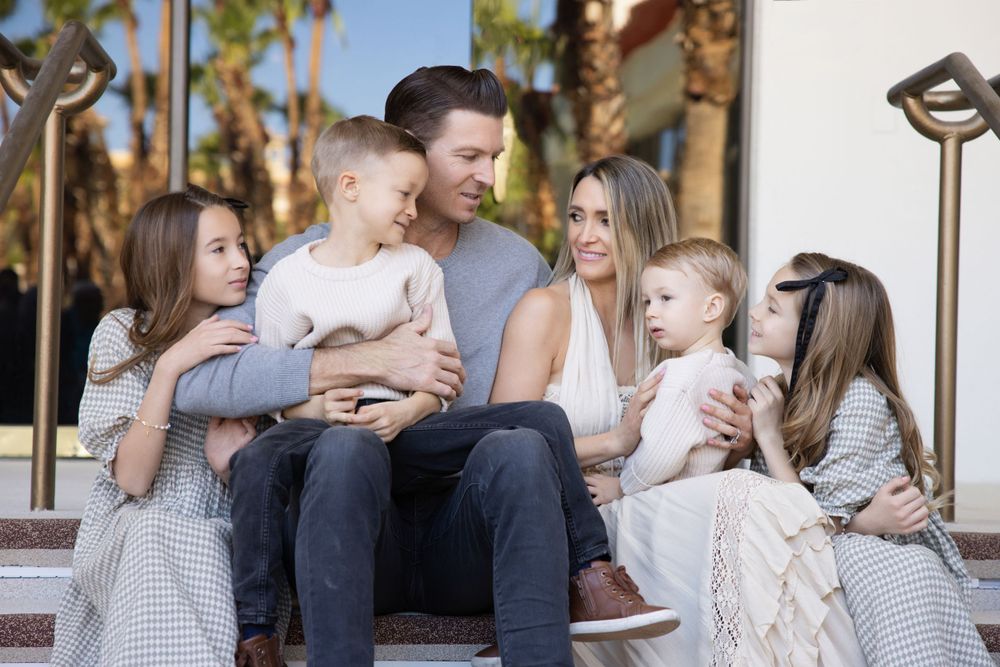 A family sits together on outdoor steps at sunset with palm trees visible in the background.