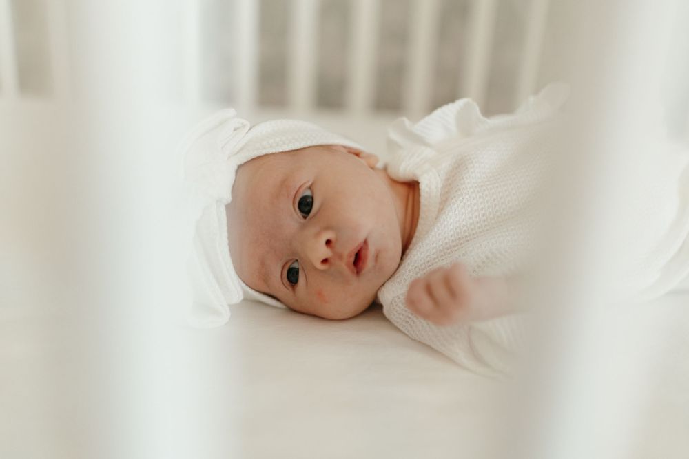 Newborn baby wearing white clothing rests on soft white bedding. Virginia/ North Carolina Newborn In-Home Session