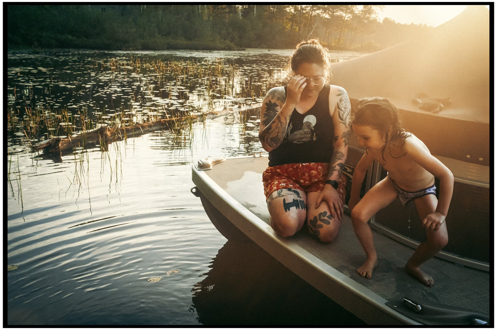 Two people sitting in a boat on calm water during golden sunset hour while leaning over the edge.