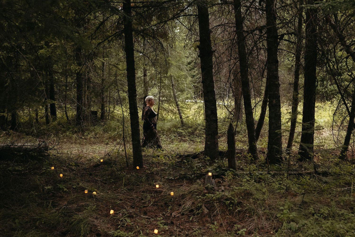 Person in black dress walking through a dark forest with glowing lights along a path. Whitney Popp. Phoenix Arizona photographer