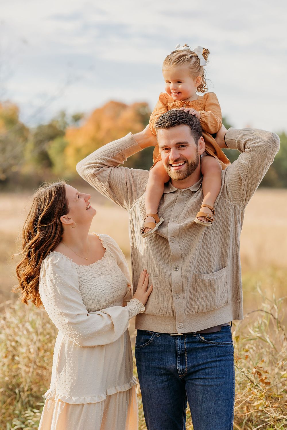 Family enjoying playful moments together in a golden autumn field during sunset.