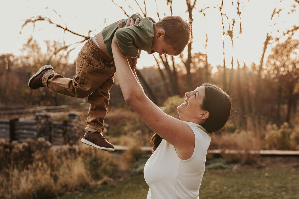 A tender moment captured during sunset as a parent lifts a small child playfully in the air.